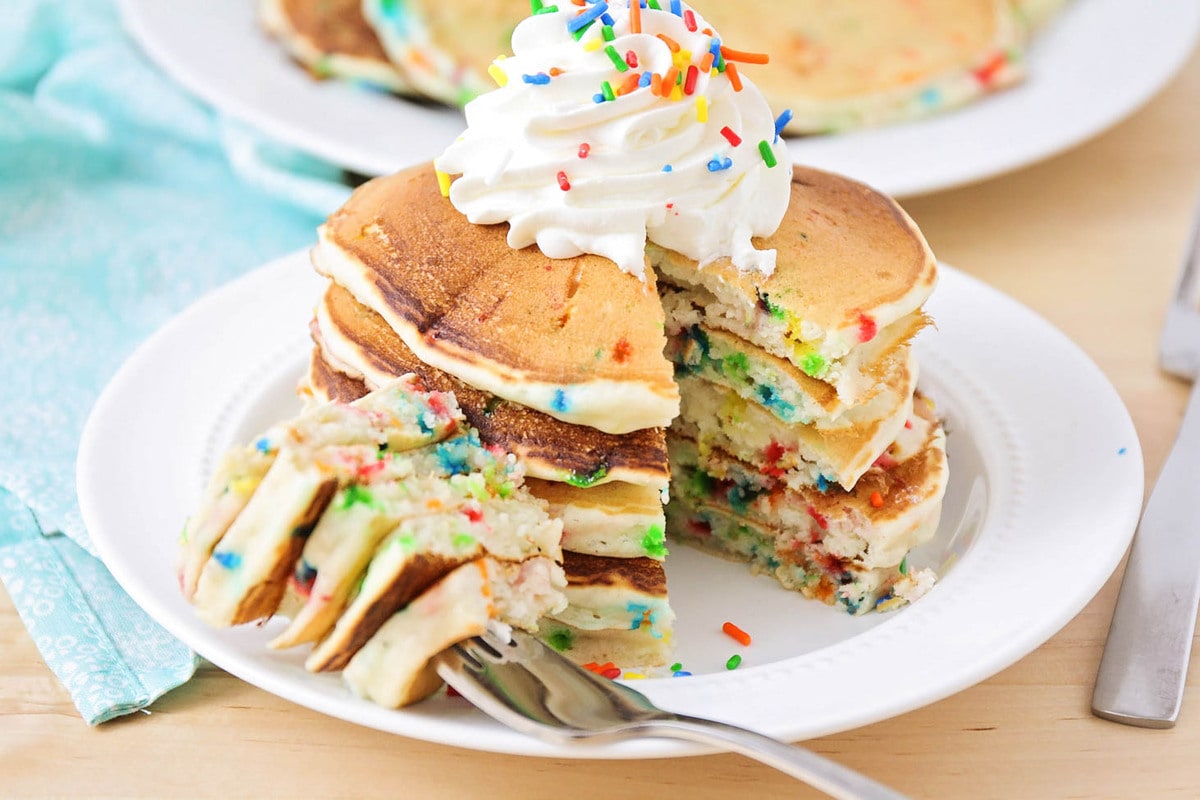 Stack of funfetti pancakes with whipped cream and sprinkles with bite taken out