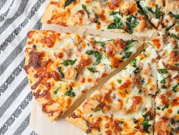 Chicken Alfredo Pizza recipe with slice cut out on cutting board.