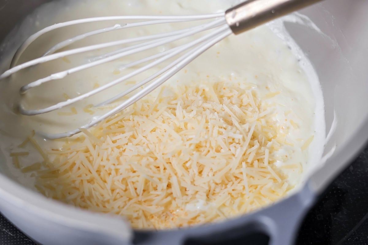 Alfredo sauce with shredded cheese in saucepan.