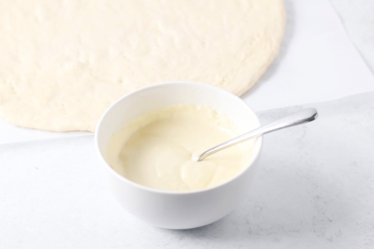 Alfredo sauce in a small white bowl for Alfredo Pizza.