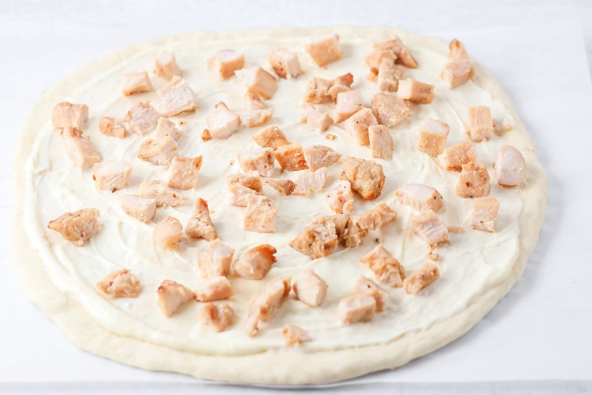 Chicken spread over white sauce pizza.