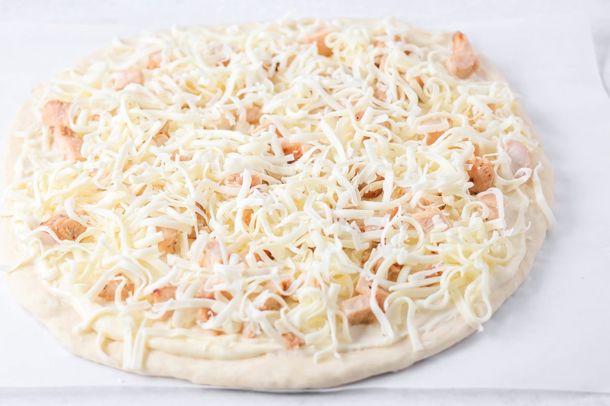 Shredded cheese spread over chicken and white sauce on pizza recipe.