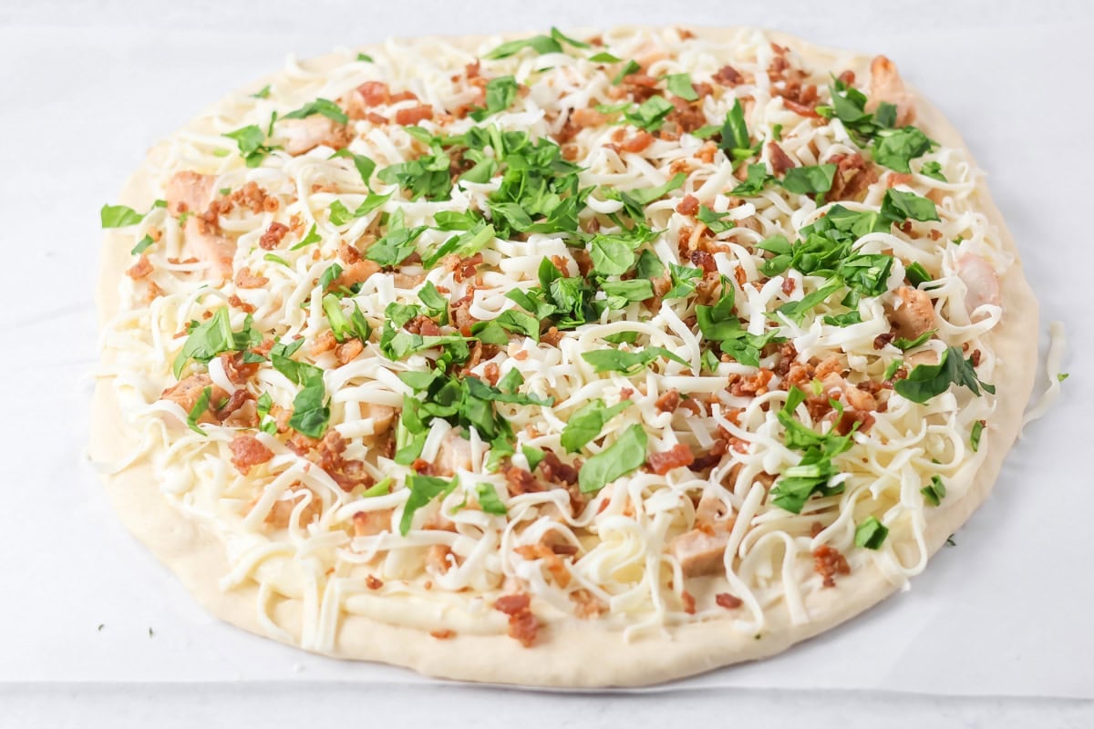 Chopped spinach spread over Alfredo pizza dough.