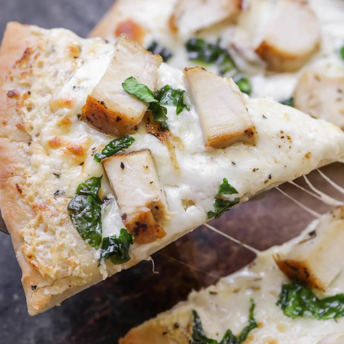 Easy Dinner Ideas - A slice of chicken alfredo pizza being pulled away from the entire pie.