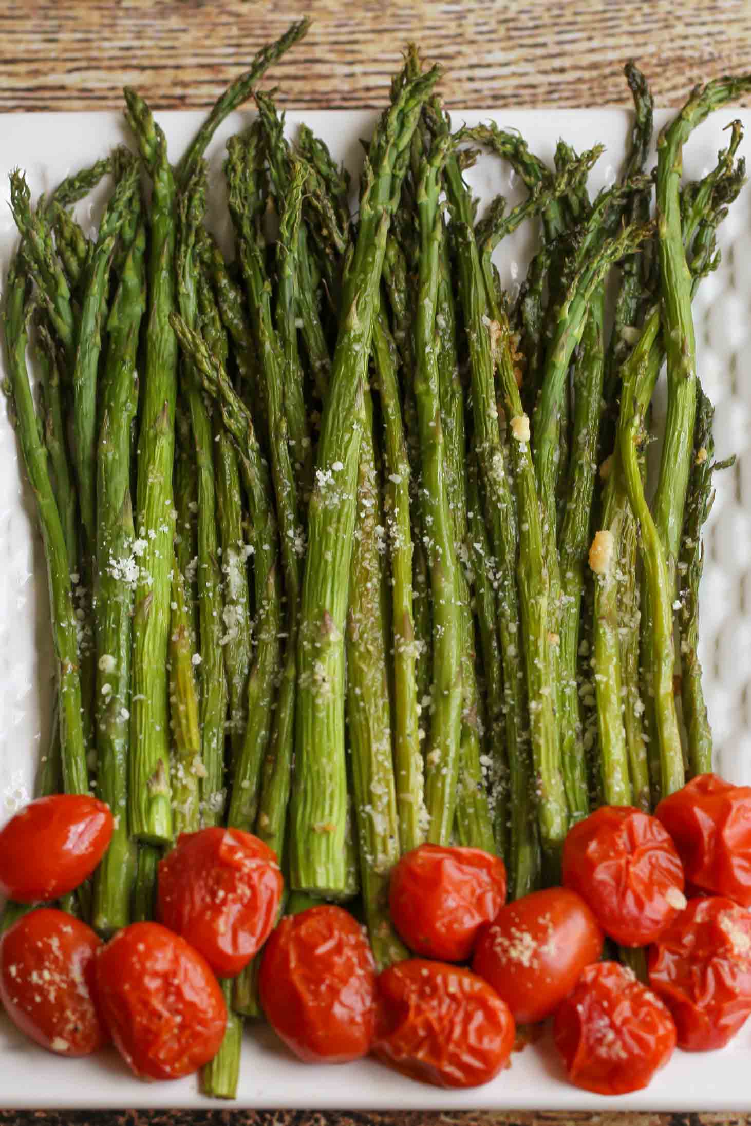 Baked parmesan asparagus on a platter with cherry tomatoes.