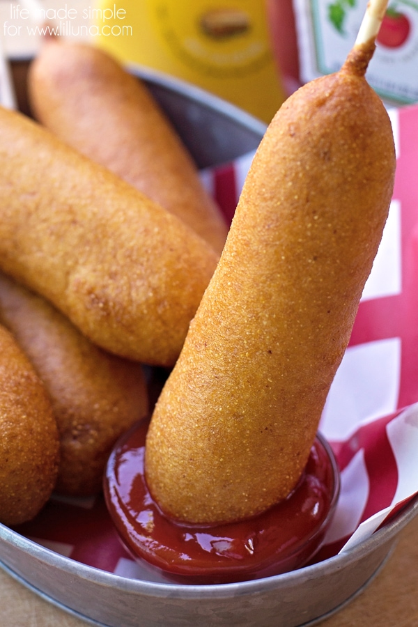 A corn dog being dipped in ketchup.