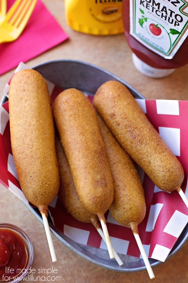 Corn dogs piled in a metal bowl served with ketchup.