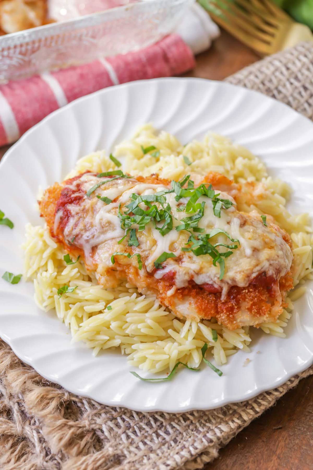 Easy Baked Chicken Parmesan on top of orzo pasta on a white plate.