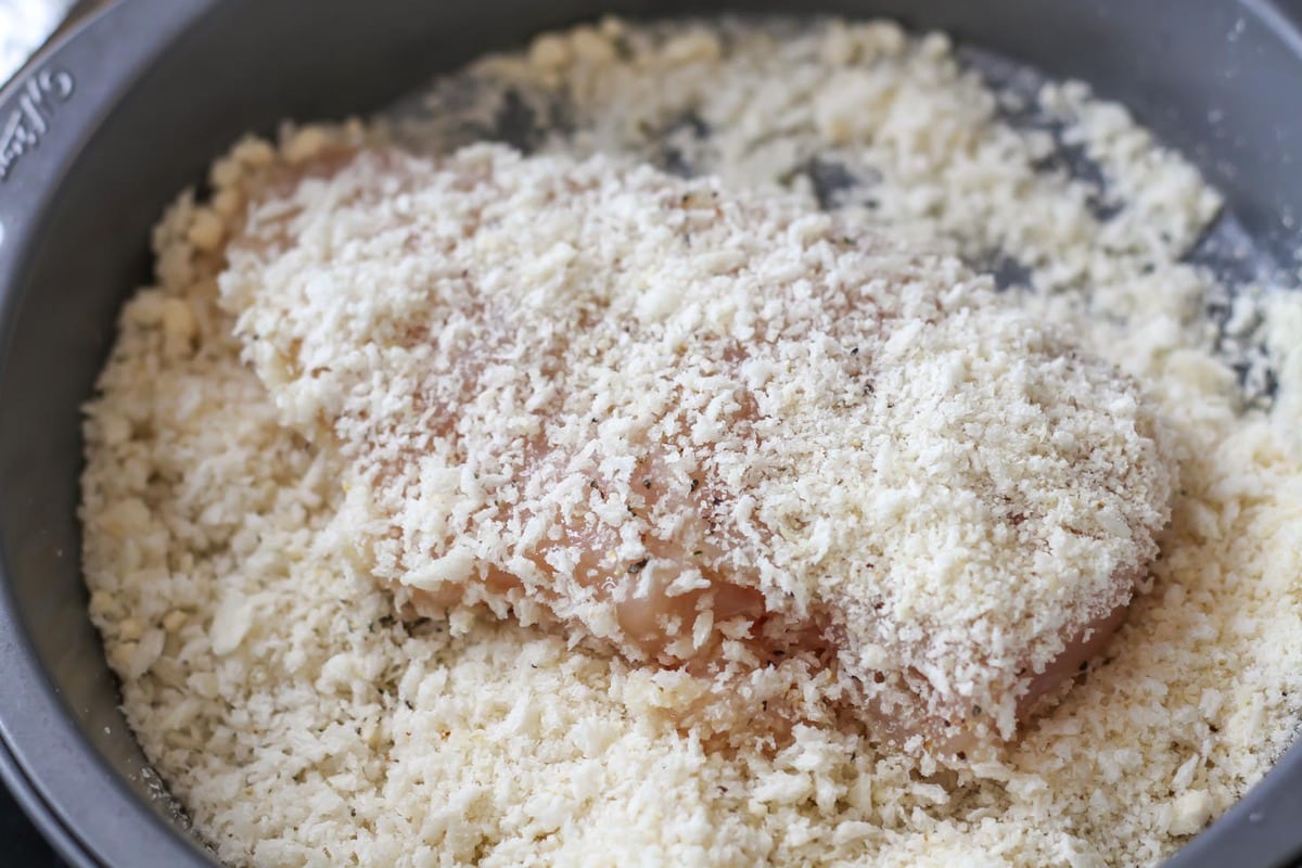 Raw chicken breast being breaded in panko.