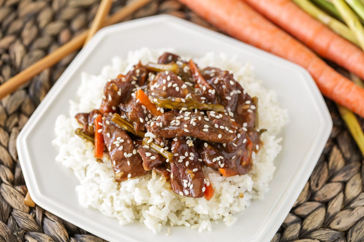 Asian Dinner Recipes - Crock Pot Mongolian Beef topped with sesame seeds on top of white rice on a white plate. 