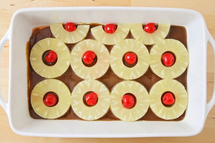 Our best pineapple upside down cake is a family favorite with a secret ingredient that takes this classic to a whole new level! Pineapple rings, sauce, and cherries in the bottom of a baking dish.