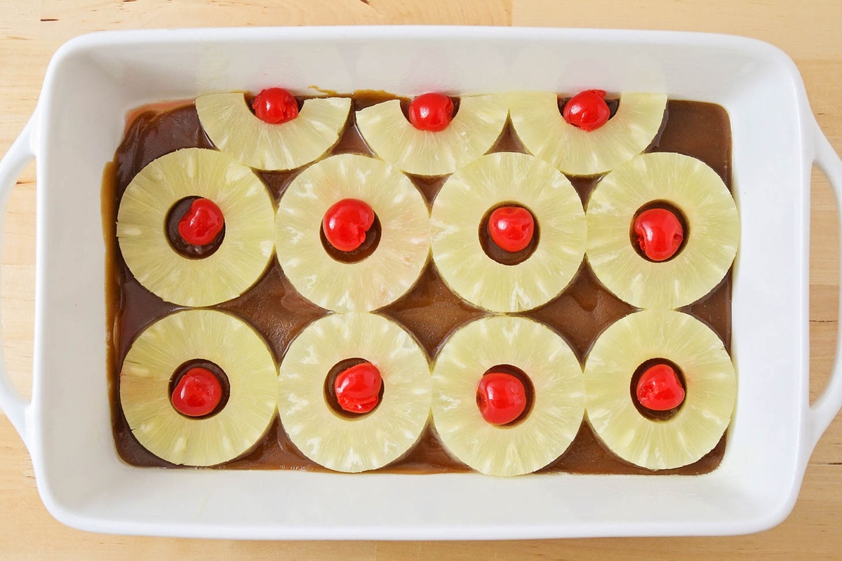 Pineapple rings, sauce, and cherries in the bottom of a baking dish.