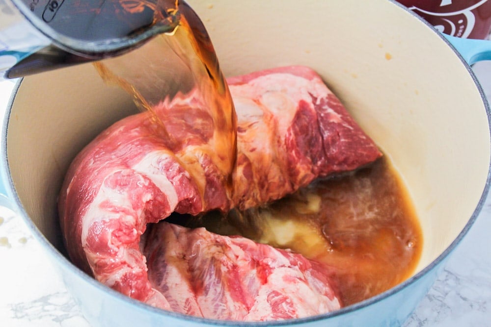 Pouring Dr. Pepper over the rack of ribs in a stock pot.