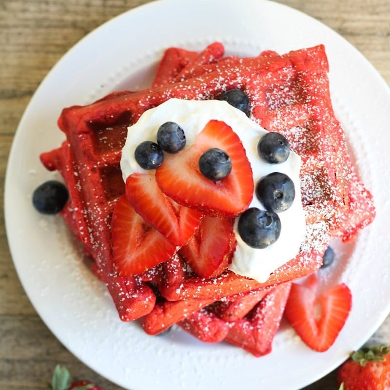 Top view of stack of Red Velvet Waffles with strawberries, blueberries and whipped cream on top.