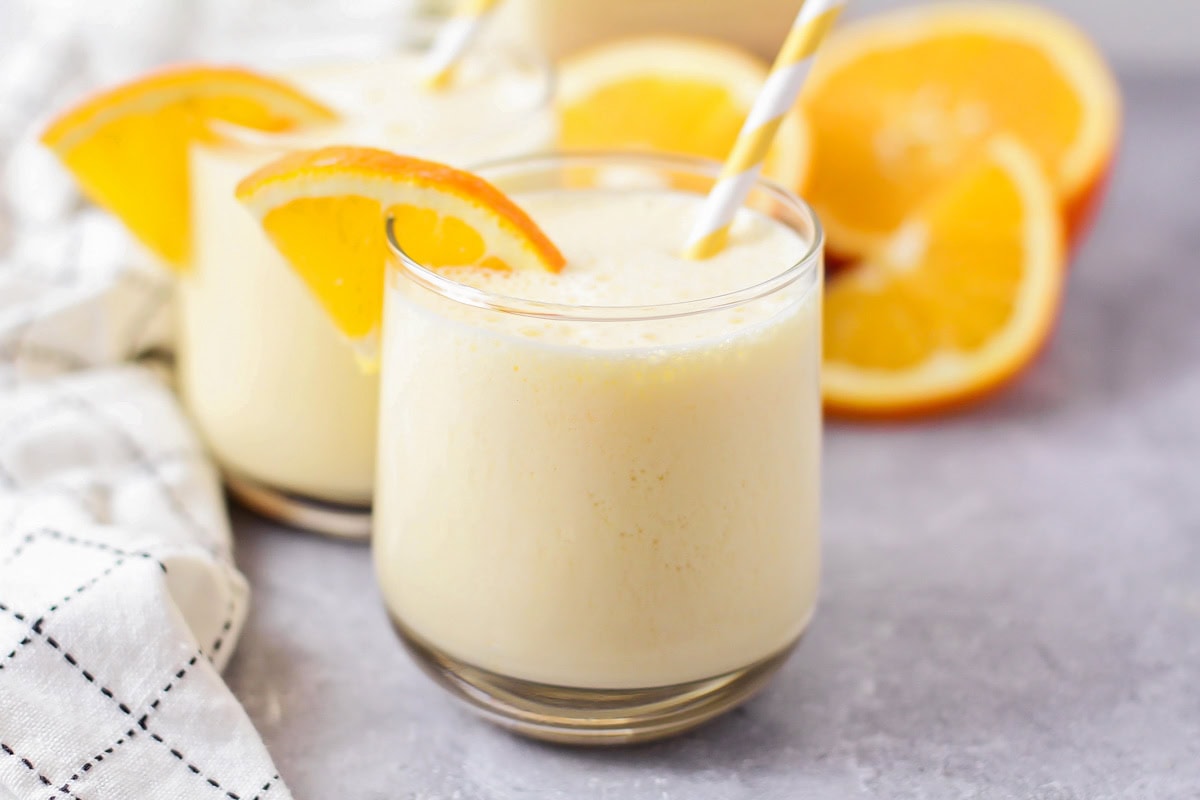 Homemade Orange Julius recipe poured into glass cup with orange slices and straw.