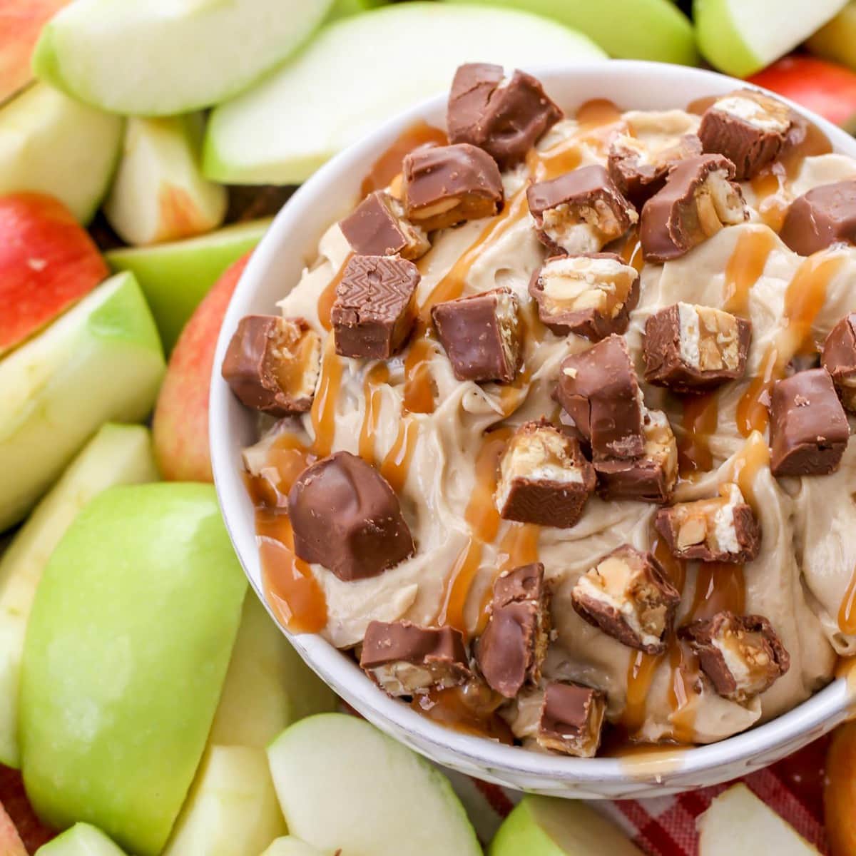 Super Bowl Appetizers - Snickers dip in a white bowl surrounded by sliced red and green apples. 