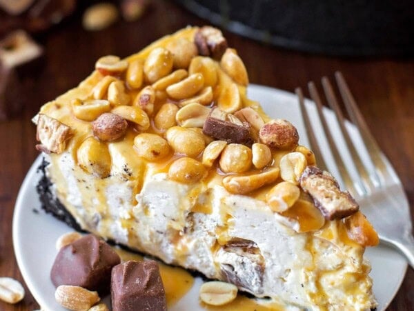 A slice of no bake snickers cheesecake on a white plate.
