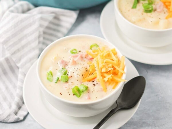 Ham and potato soup recipe with cheese on top with spoon on the side.