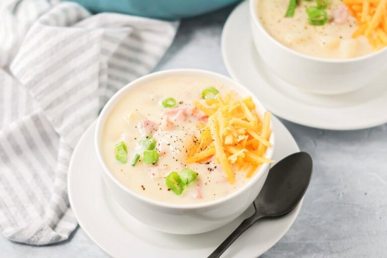 Ham and potato soup recipe with cheese on top with spoon on the side.