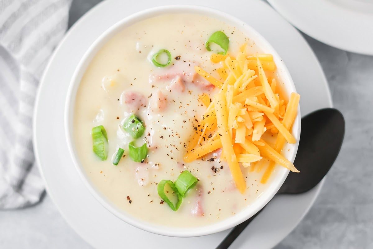 A bowl of ham and potato soup topped with shredded cheese and scallions.