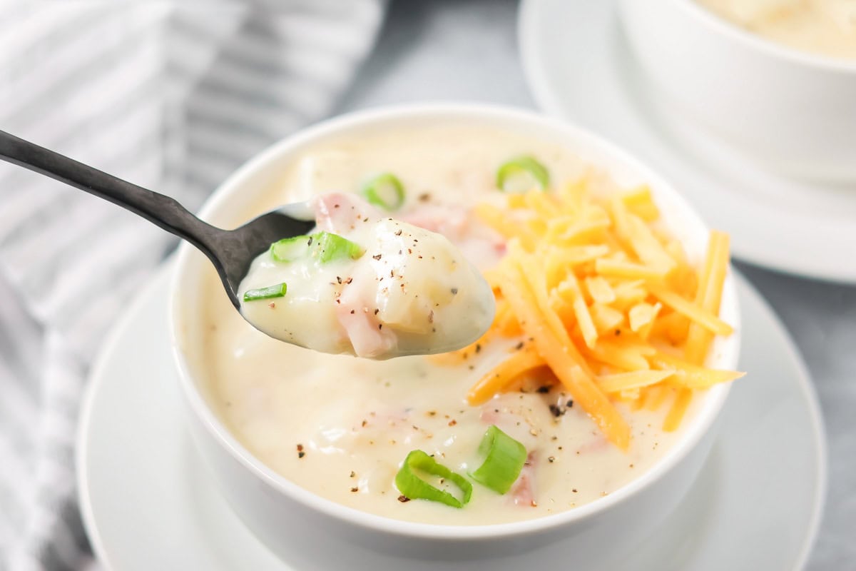 A spoon full of ham and potato soup topped with fresh pepper.