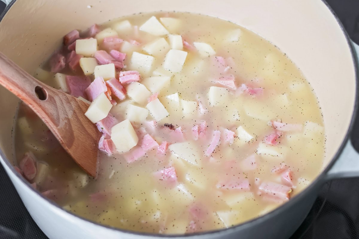 Stirring diced ham and potatoes in a pot on the stove.