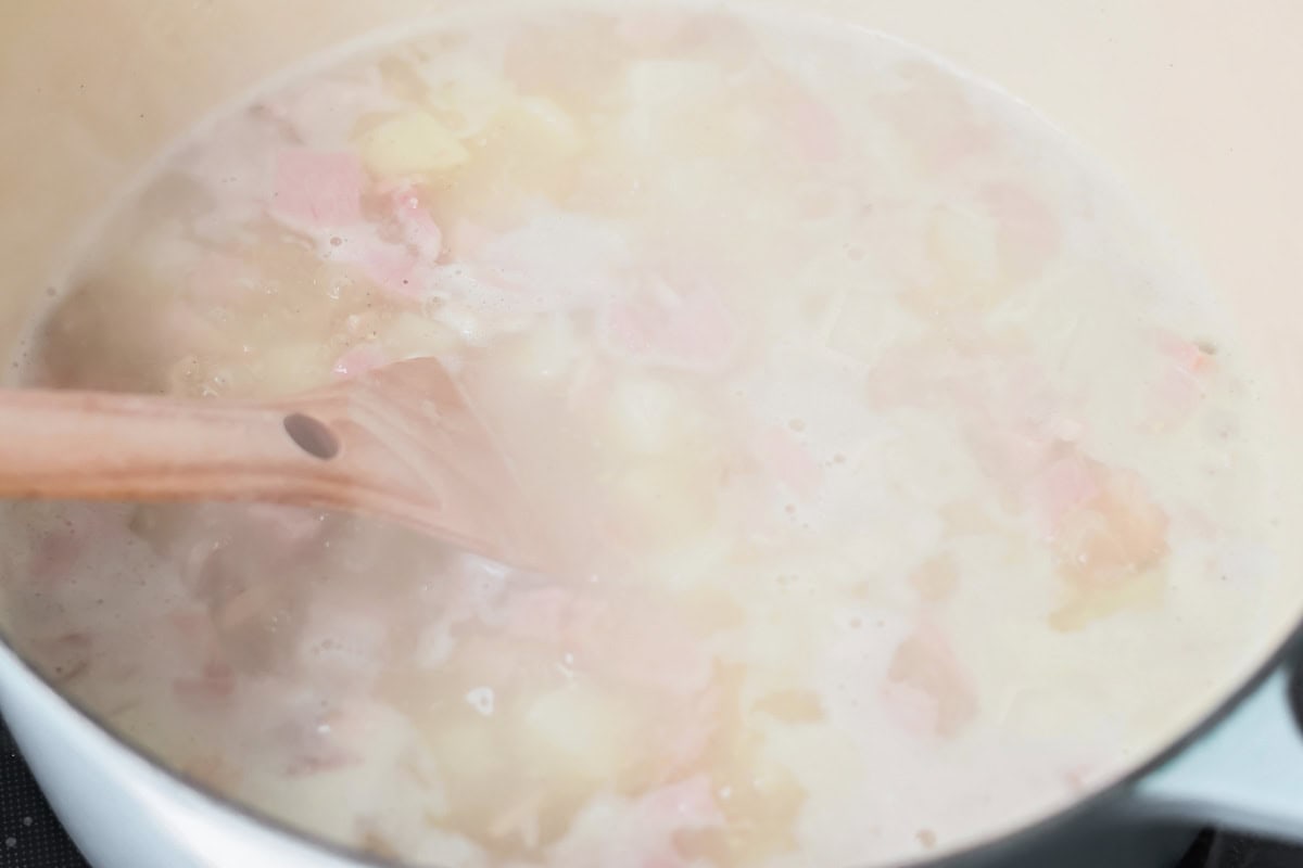 Stirring ham and potato soup in a durtch oven on the stove.