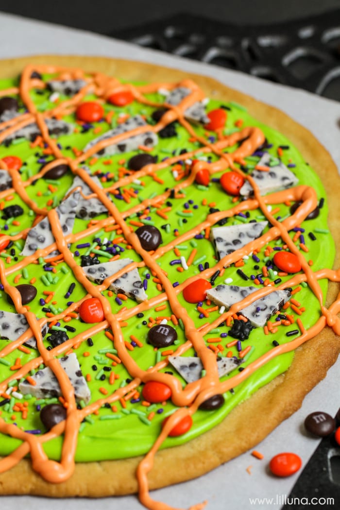 Halloween sugar cookie cake with green and orange frosting and candy.