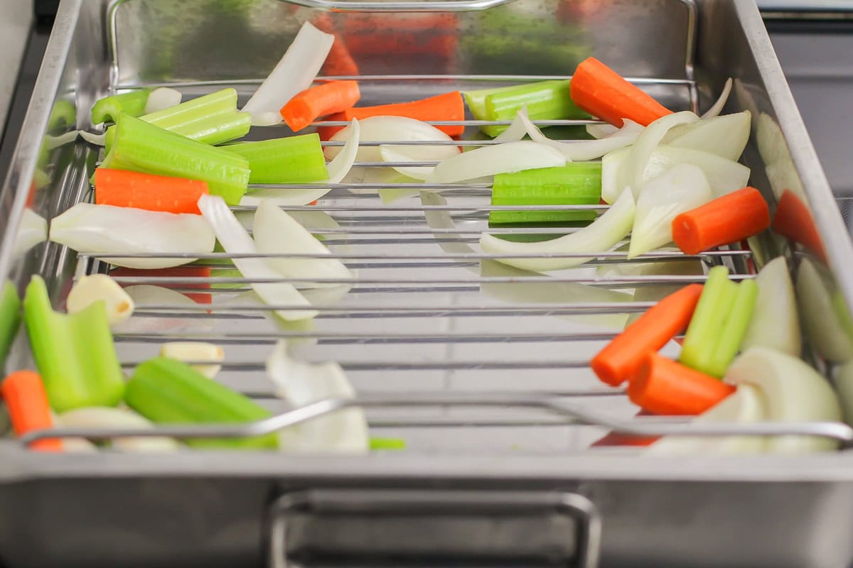 Vegetables sprinkled into the bottom of a roasting pan.