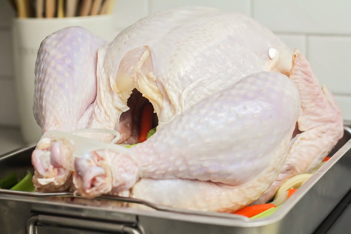 Veggies inserted into the cavity of a turkey in a roasting pan.