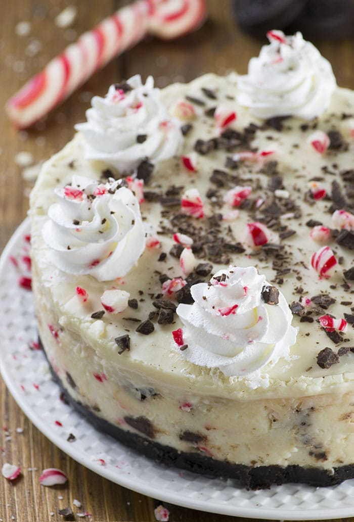 Peppermint Bark Cheesecake - It has three delicious layer-Oreo crust, creamy cheesecake filling loaded with peppermint bark pieces and white chocolate ganache on top garnished with crushed candy canes, whipped cream and chocolate.