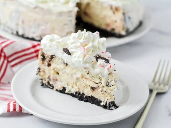 Peppermint Cheesecake slice on plate with whipped cream and crushed candy canes on top.