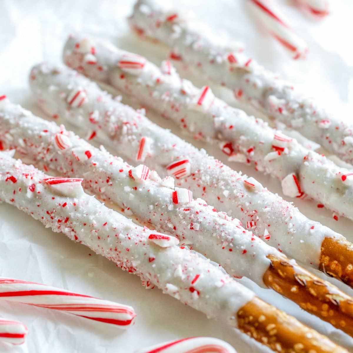 Candy cane coated white chocolate peppermint pretzel rods on was paper.