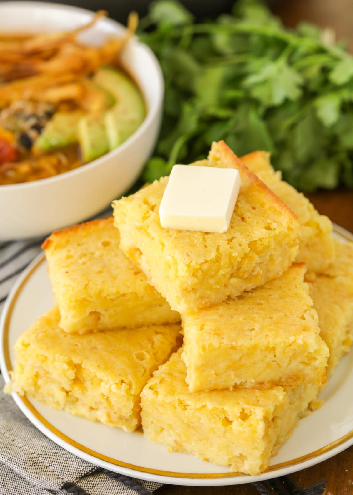 Sweet cornbread stacked on a white plate topped with butter