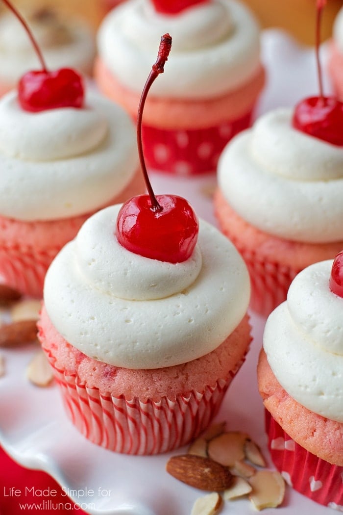 Cherry almond cupcakes with a cherry on top, displayed on a white plate.