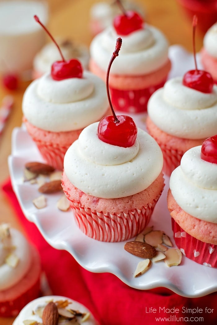Cherry almond cupcakes topped with maraschino cherries displayed on a white plate.
