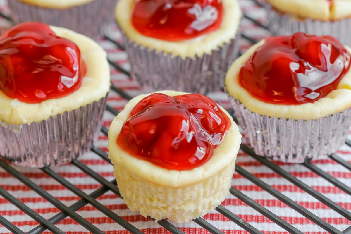 Mini cherry cheesecakes in cupcake liners on a wire rack