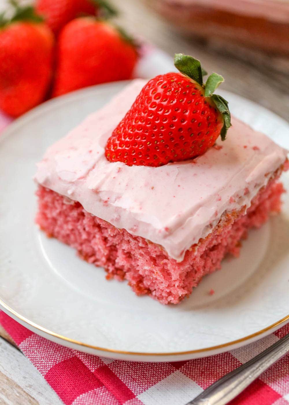 Strawberry sheet cake recipe on plate topped with a fresh strawberry.