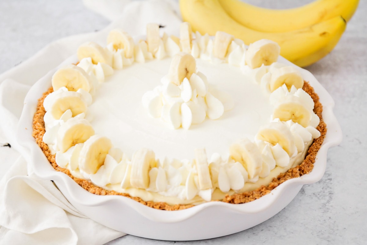 Banana pudding cheesecake in a baking dish topped with whipped cream and banana slices. 