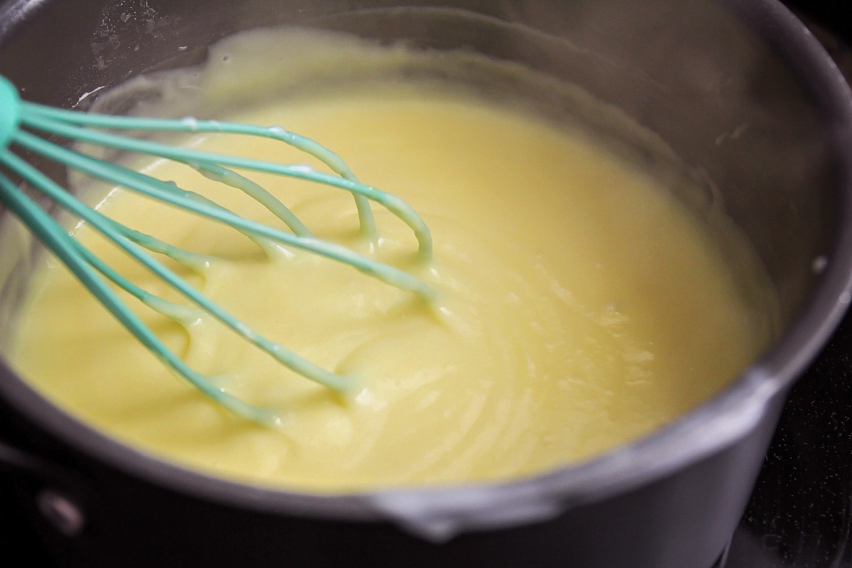 Banana pudding cheesecake filling mix in a metal bowl being whisked with a teal whisk. 
