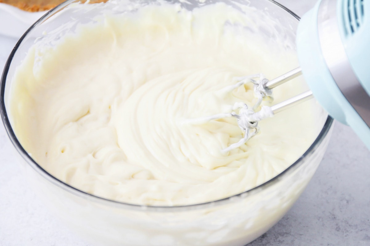 No bake cheesecake filling being mixed in a glass bowl with a hand mixer.