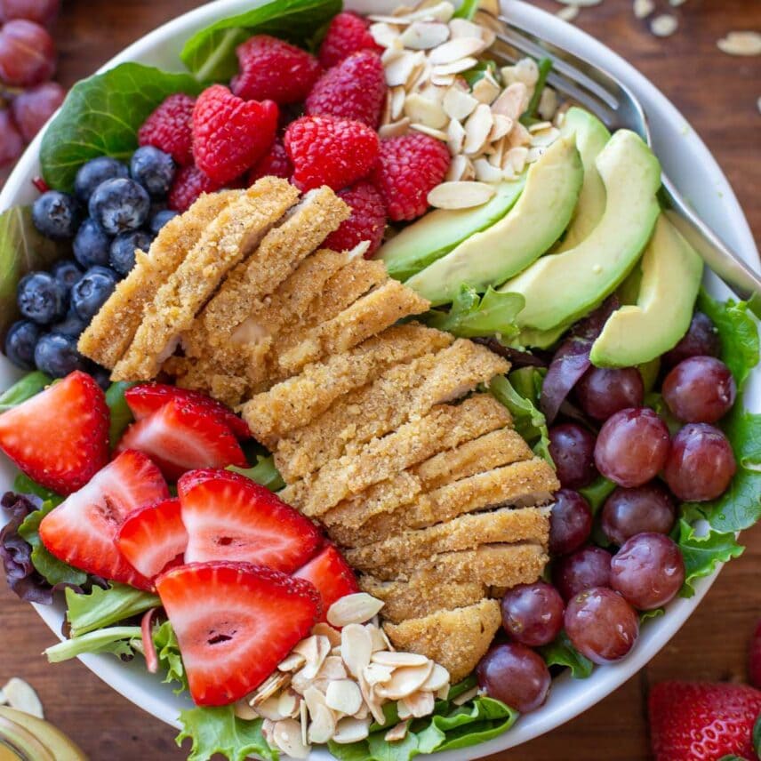 A photo of honey mustard chicken salad topped with fruit and avocado.