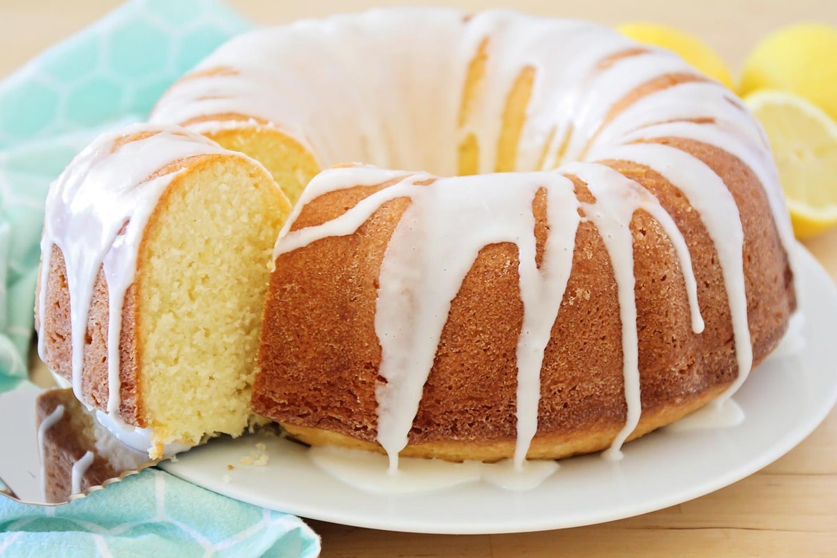 A glazed lemon pound cake with a slice being removed.