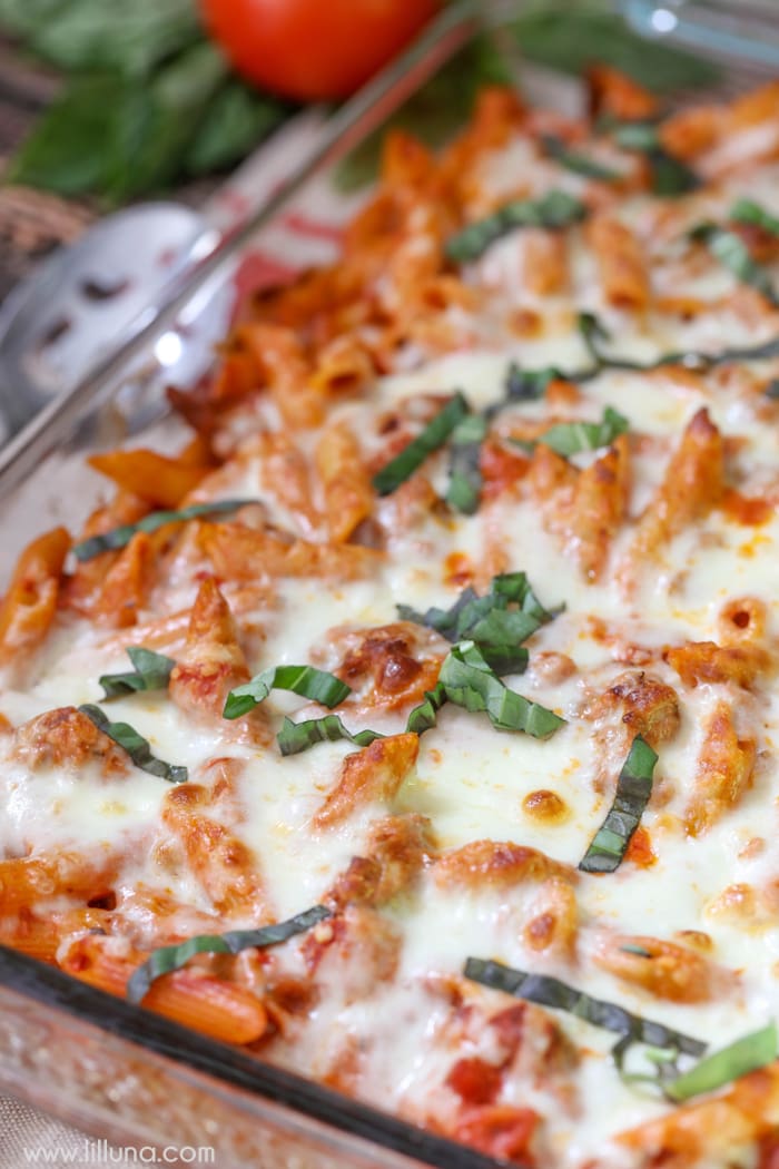 Creamy Sausage Penne Bake topped with fresh basil in a glass baking dish