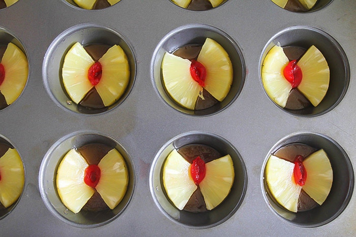 pineapple and cherry slices in the bottom of a cupcake tin