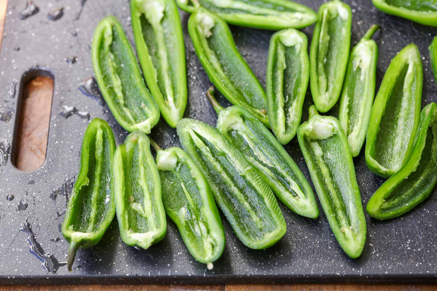 Cut, halved and seeded jalapenos on a black cutting board.