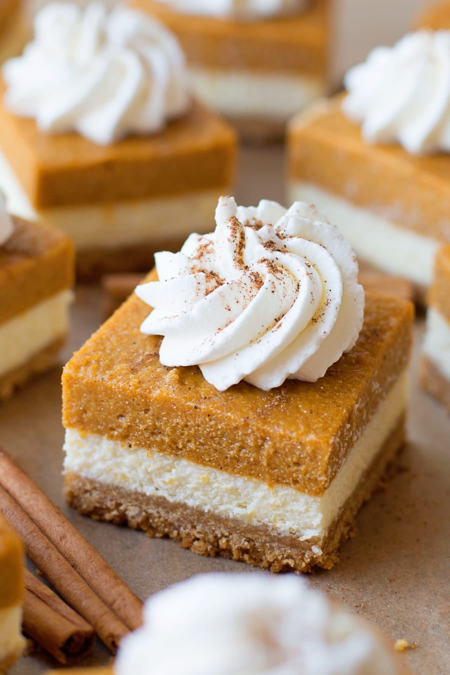 Sliced pumpkin pie cheesecake bars topped with a dollop of whipped cream.