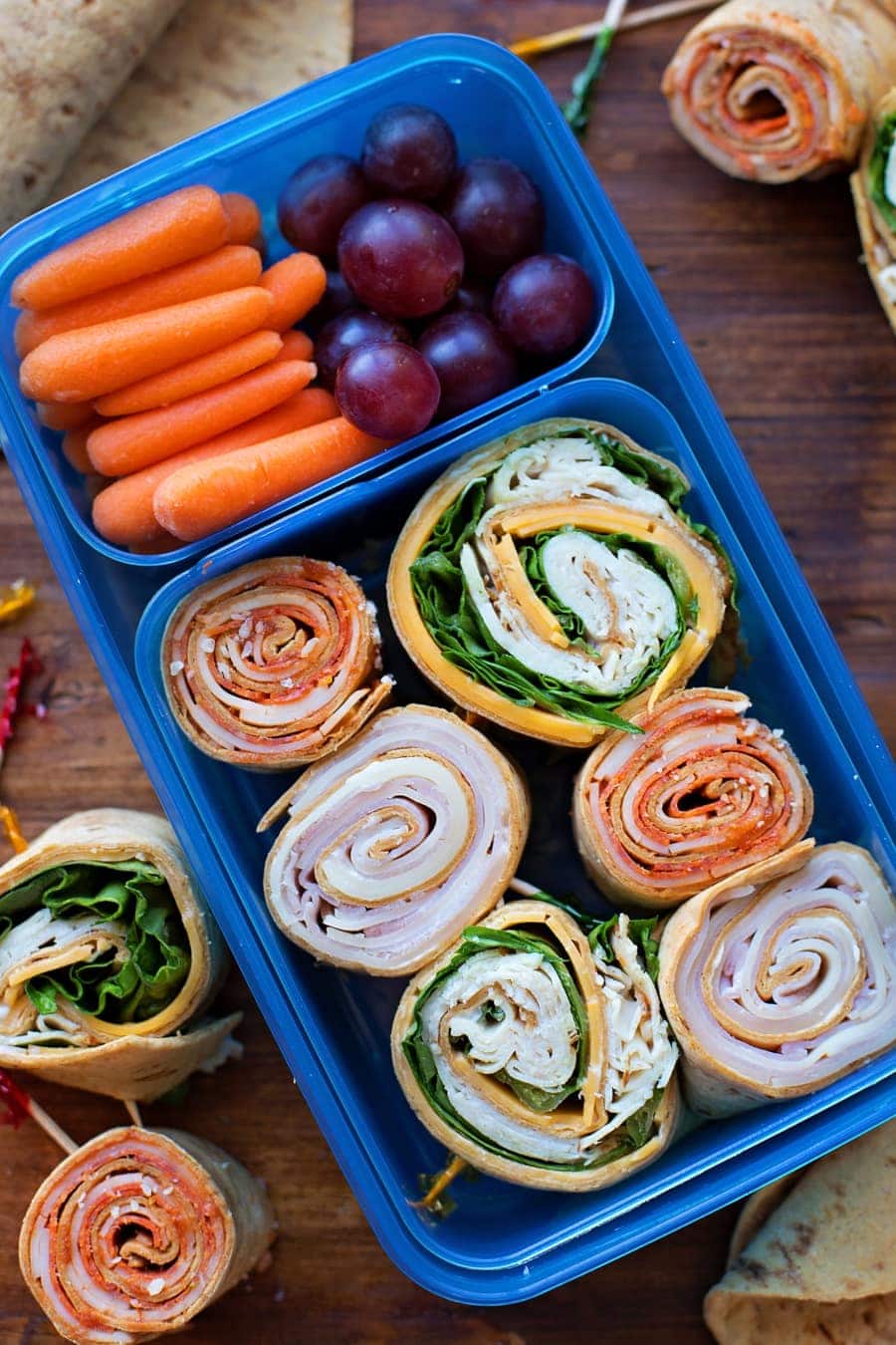 rolled flatbread pinwheels in a container with carrots and grapes