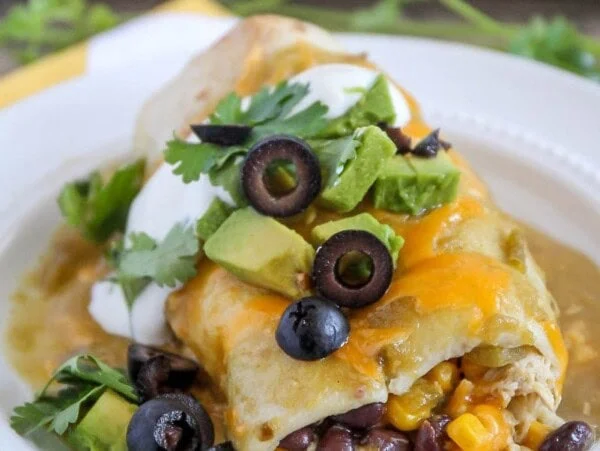 green chili smothered burrito with olives, cilantro and avocado on plate