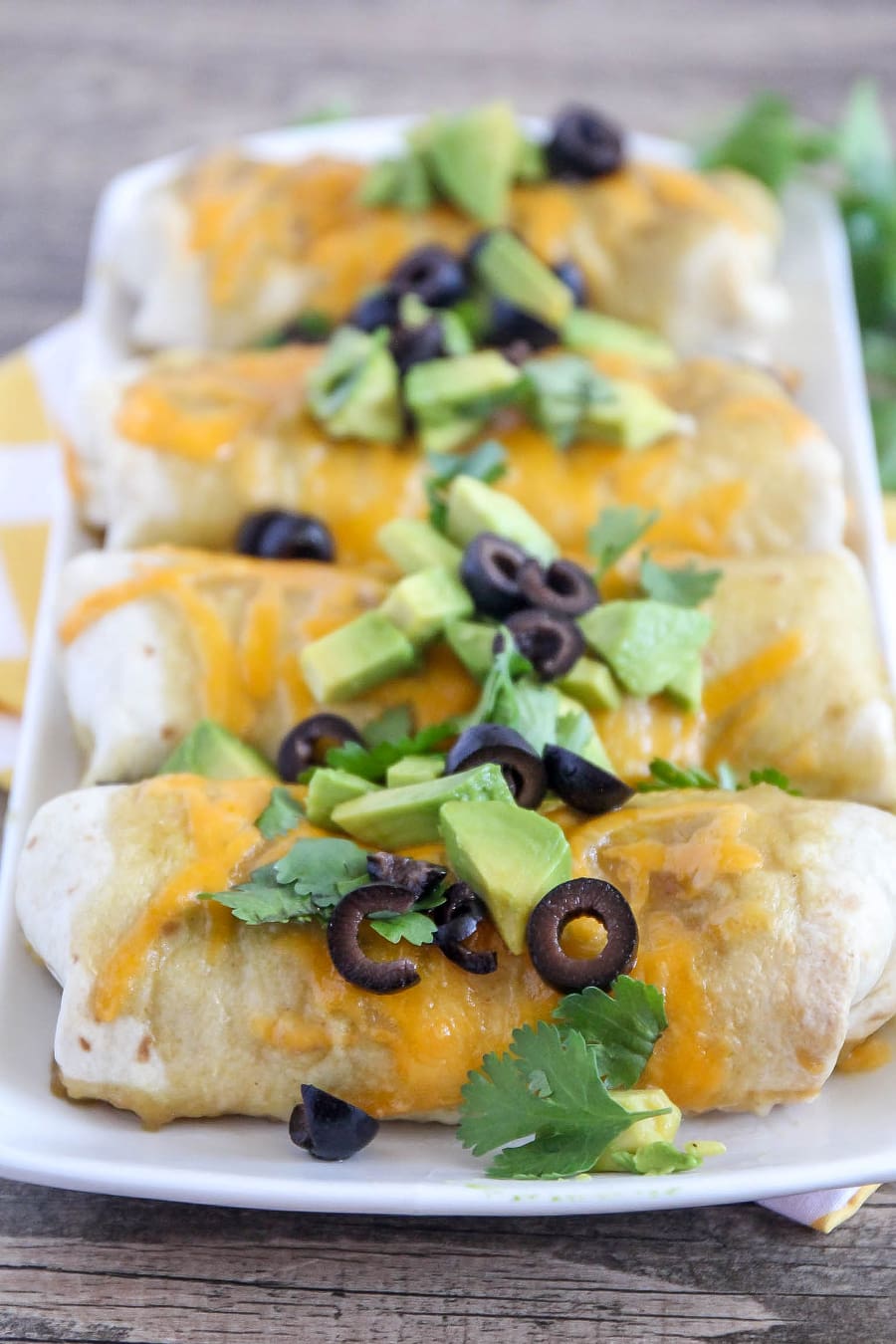 Green Chili Burritos topped with cilantro, avocado and olives on a white platter